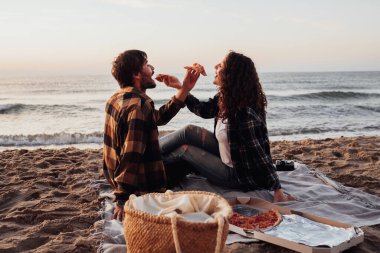 Woman and man eating pizza by the sea, young couple having a picnic and meeting dawn on beach