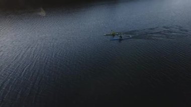 Gün batımında göl kenarındaki kanoda yüzen iki tanınmayan insanın hava görüntüsü.