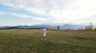 Elinde yeni doğmuş bir bebekle arka planda dağlara karşı yürüyen tanınmayan bir kadının hava görüntüsü, insansız hava aracı ileri uçuyor.