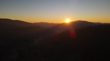 Karpatlar 'ın dağları üzerinde gün batımının inanılmaz manzarası. İnsansız hava aracı yavaşça geriye doğru uçuyor ve güneş dağların üzerinde parlıyor.