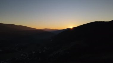 Dağların üzerinden gün batımının manzarası, insansız hava aracı uçuyor ve güneş dağın arkasında beliriyor.
