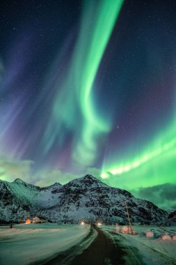Aurora Borealis, Norveç 'in Flakstad, Lofoten adalarında kış günü kar dağı ve yol üzerinde Kuzey Işıkları patlaması