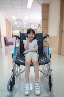 Hastanede gülümseyen ve tekerlekli sandalyede parmağını kaldıran Asyalı tatlı kız.