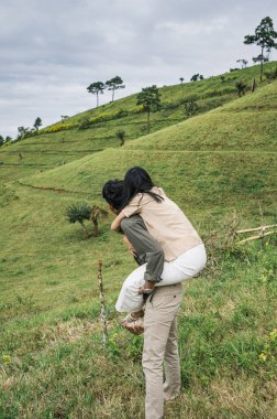 Romantik genç Asyalı çift tatilde kırsal yamaçta çayırlarda gezintiye çıkıyor.