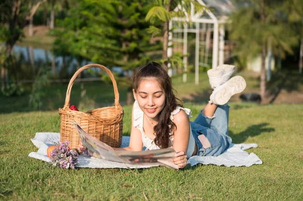 Young asian woman picnic with reading newspaper on cloth in the garden on summertime