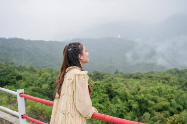 Asyalı bir kadının sırtı, yağmur mevsiminde sisli dağ manzarasıyla dinleniyor ve bakıyor.