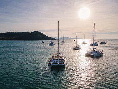Gün batımında tropikal denizde yelken açan bir grup özel yatın hava görüntüsü.