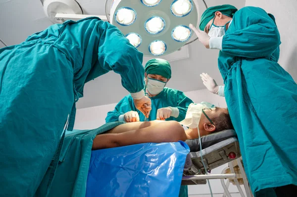 一名身穿外科礼服的亚洲外科医生小组在医院手术室为一名重伤员做手术 — 图库照片