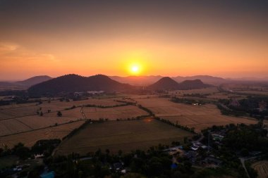 Dağların üzerinden renkli günbatımının havadan görünüşü ve kırsal kesimdeki tarlalarda çeltik tarlaları.