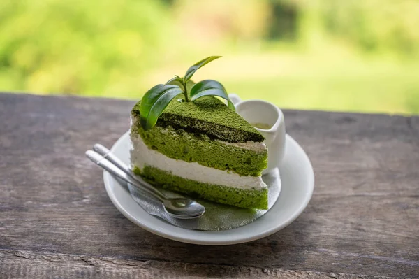プランテーションの木製バーで白い皿にホイップクリームと茶葉をスライスした有機緑茶ケーキ — ストック写真