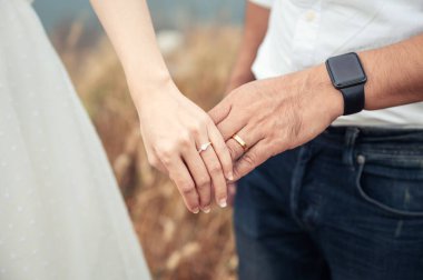Gelin ve damat düğün öncesi gün ormanda alyansla el ele tutuşuyorlar. Gelinlik, evli çift.
