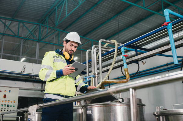 Caucasian technician engineer man in uniform with tablet checking and control boiler tanks and liquid pipeline in chemical factory production line