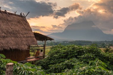Genç turist çift, Chiang Dao, Chiang Mai, Tayland 'daki Doi Luang Chiang Dao dağının üzerinde, ahşap kulübenin balkonunda ve günbatımında oturuyorlar.