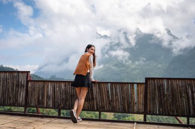 Çekici Asyalı kadın, Chiang Dao, Chiang Mai 'de güneşli bir günde tahta balkonda durup dağ manzarasının keyfini çıkarıyor.