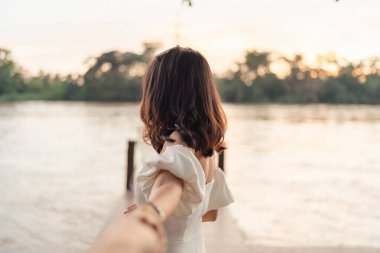 Beyaz gelinlikli gelin, nişanlısıyla el ele tutuşuyor. Arka plan bulanık. Akşamları doğa arasında.