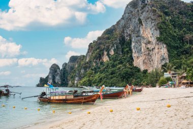 Tayland, Krabi 'de güneşli bir günde Phi Phi adasında sahile demir atmış ahşap uzun kuyruk teknesi ve kireçtaşı dağı.