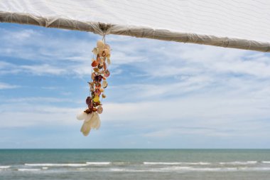 Güneşli bir günde tropik plajlı ahşap çardakta asılı deniz kabuğu hatırası.