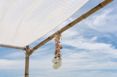 Güneşli bir günde tropik plajlı ahşap çardakta asılı deniz kabuğu hatırası.