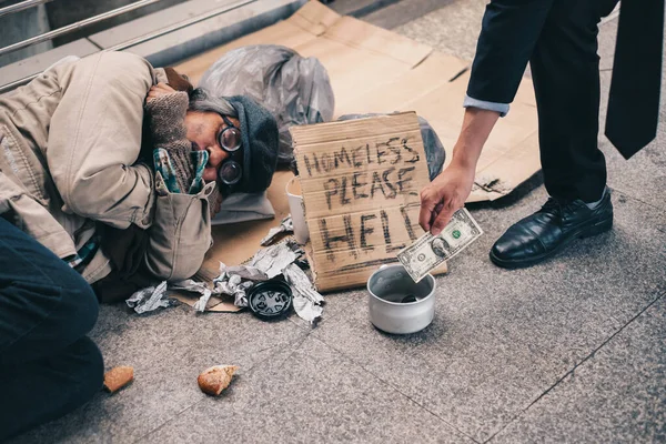 商人给捐赠美元现金与睡觉的老无家可归的人 — 图库照片