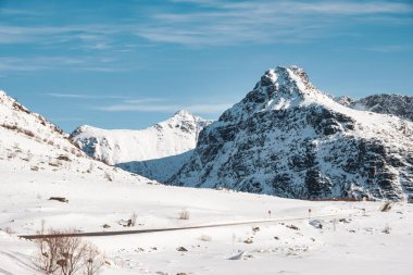 Norveç 'in Lofoten adalarındaki güneşli bir günde karlı dağ sırasının ve kışın yol manzarası
