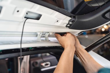 Tamircinin eli takozu söküp garajdaki bir arabaya kamera yerleştiriyor.