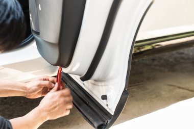 Tamircinin eli takozu söküp garajdaki bir arabaya kamera yerleştiriyor.