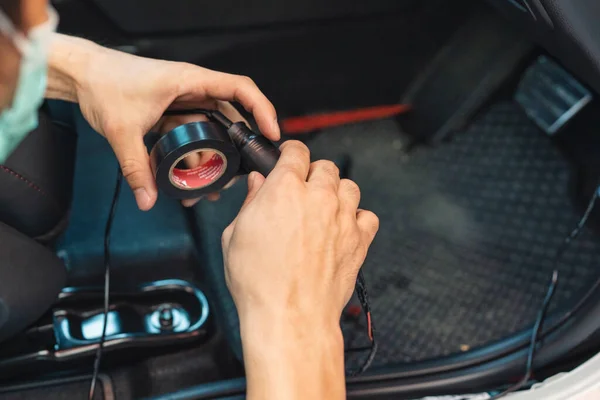 Hand of mechanic using duct tape wrapping wire of car to install electronic device