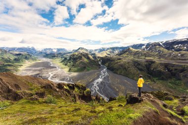 Scenery of Valahnukur viewpoint with female hiker standing on peak and krossa river flowing through in icelandic highlands at Thorsmork, Iceland