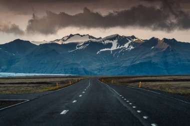 Dramatic straight asphalt road with storm over mountain on gloomy day in Iceland