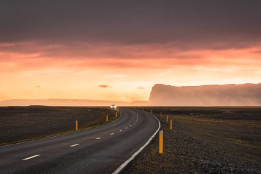 Scenic curved asphalt road with car driving and sunset sky on mountain in summer of Iceland 