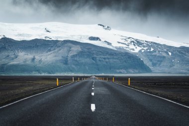 Dramatic straight asphalt road with storm over mountain on gloomy day in Iceland