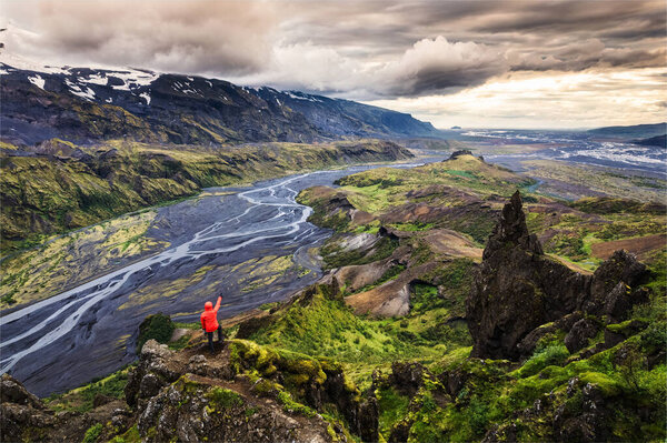 Scenery of Hiker man in red jacket standing on peak of Valahnukur viewpoint with mountain valley and krossa river in icelandic highlands at Thorsmork, Iceland