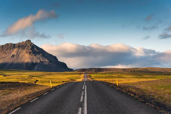 Scenic empty asphalt straight road with sunlight shining and mountain view in summer of Iceland