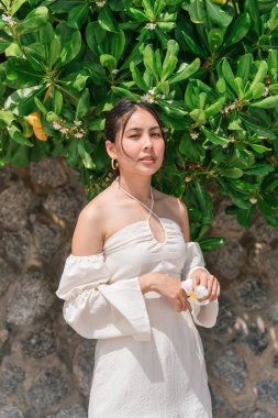 Yeşil yapraklar üzerinde poz veren güzel Asyalı kadın tropik adada bitki yetiştiriyor.