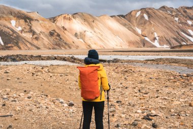 Sarı ceketli kadın sırt çantalı. İzlanda 'nın dağlık kesimlerinde yaz mevsiminde Landmannalaugar yolunda duruyor.