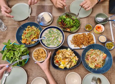 Tayland yemeğinin çeşitli çeşitleri papaya baharatlı salata, meyve salatası, kıtır domuz eti, baharatlı domuz çorbası, Tayland restoranındaki ahşap masada yapışkan pirinç ve çatal bıçak.