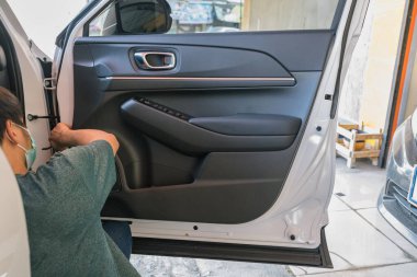 Tamirci, garaj atölyesinde araba sorununu kontrol etmek için araç kapısını açıyor.