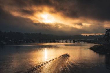 Mon ahşap köprüsü üzerinde güzel bir gün doğumu ve Songkalia nehri üzerinde geleneksel bir tekne ve Sangkhlaburi, Kanchanaburi, Tayland 'da yerel bir köy.