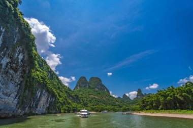 Çin 'in Guilin ve Yangshuo kasabaları arasında akan görkemli Li nehri üzerinde karst dağlarının yüksek dikey uçurumlarında seyahat eden turistleri taşıyan bir tekne.