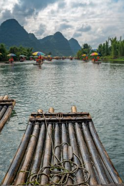 Çin 'in Yangshuo kentindeki Yulong Nehri' nin manzaralı ve güzel rehberleri tarafından yönetilen turistleri taşımak için bambu salını kapatın.