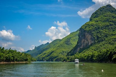 Çin 'in Guilin ve Yangshuo kasabaları arasında akan görkemli Li nehri üzerinde karst dağlarının yüksek dikey uçurumlarında seyahat eden turistleri taşıyan bir tekne.