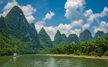 Çin 'in Guilin ve Yangshuo kasabaları arasında akan görkemli Li nehri üzerinde karst dağlarının yüksek dikey uçurumlarında seyahat eden turistleri taşıyan bir tekne.