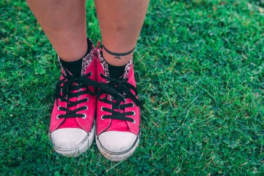 Pembe spor ayakkabılı bir kız taze yeşil çimlerin üzerinde duruyor.