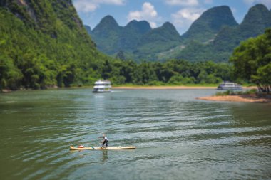 Yangshuo, China - August 2019 : Old fisherman paddling on a small narrow wooden boat among stunning karst mountain scenery on the magnificent Li river