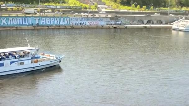 Kijów, Ukraina - 24 kwietnia 2021: Łódź wycieczkowa płynie wzdłuż rzeki do portu rzecznego. Łódź z turystami płynie wzdłuż szerokiej rzeki. Widok na transport wodny z brzegu. Zbliżenie — Wideo stockowe