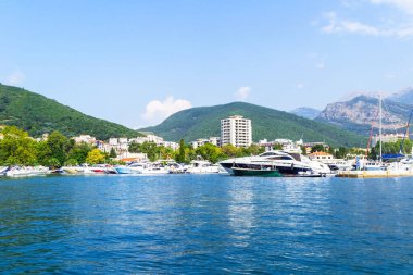 Budva şehrini bir yattan yakından çek, arka planda bitki örtüsü olan bir dağ sırası. Karadağ kıyıları boyunca seyahat et.