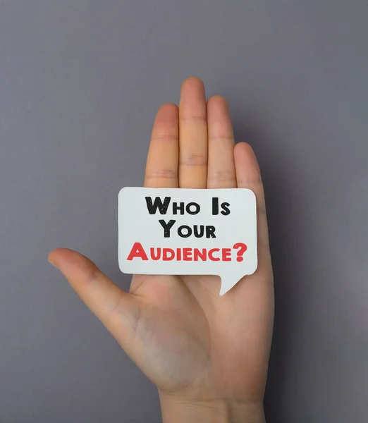 Ženská ruka na šedém pozadí drží kartu s textem Kdo je vaše publikum. Marketing a obchodní koncepce. Stock Snímky