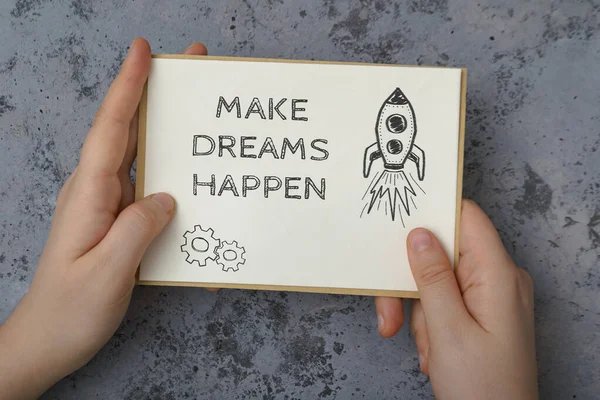 La niña sostiene una carta en sus manos con el texto Make Dreams Happen. Cita motivacional escrita en un papel blanco. —  Fotos de Stock