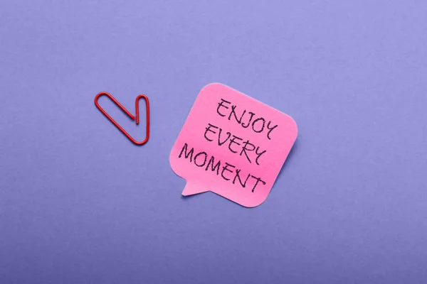 Paper with text Enjoy Every Moment on violet background — Stock Photo, Image