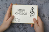 Žena ruce drží kartu s textem Nová volba na vzorovaném šedém pozadí detailní. Nová příležitost k osobnímu růstu. Koncept úspěchu a náhody